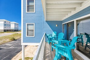 A blue building with a covered porch, outdoor seating, and a view of other buildings. - Sea Oats 105h 3 Bedroom Condo (Gulf Shores)