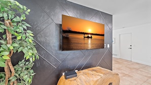A modern living room with a large flat-screen TV mounted on a textured wall, a wooden coffee table, and a potted plant. - Sarasota Solitude 3 Bedroom Home (Sarasota)