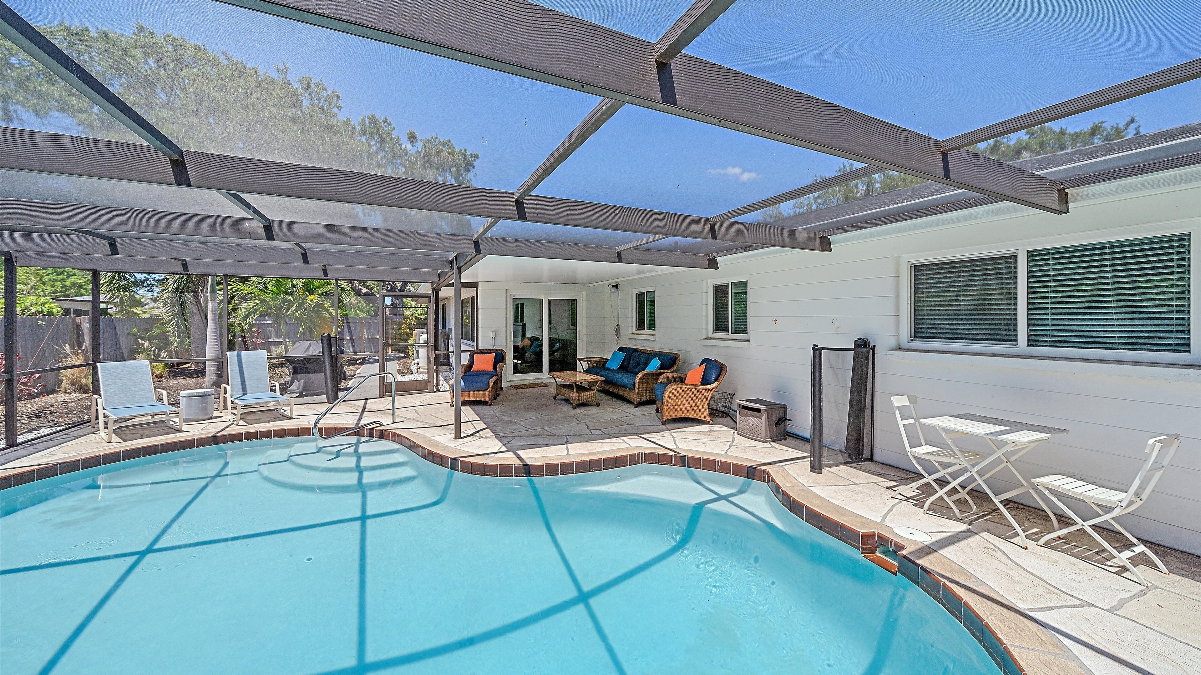 A covered outdoor swimming pool area with lounge chairs, a sofa, and a patio table.