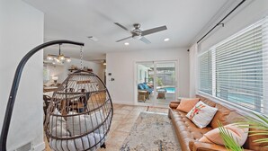 A spacious living area with a large window, a ceiling fan, and a hanging chair. - Sarasota Solitude 3 Bedroom Home (Sarasota)