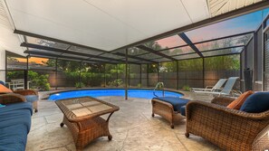 A covered outdoor area with a swimming pool, wicker furniture, and a view of the surrounding greenery. - Sarasota Solitude 3 Bedroom Home (Sarasota)