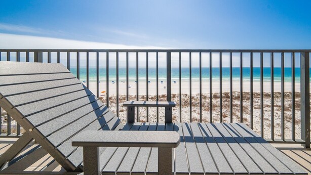 A beach view from a balcony with a railing, a bench, and a lounge chair.