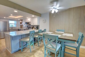A modern kitchen with a central island, dining area with blue chairs, and a clock on the wall.