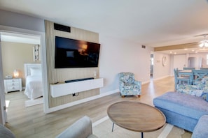 A modern living room with a flat-screen TV mounted on a wall, a round wooden coffee table, a blue sofa, and a patterned armchair. - 146 El Matador 2 Bedroom Condo (Fort Walton Beach)