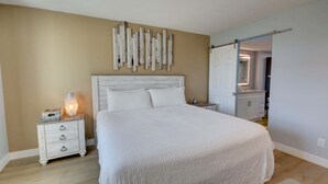 Ein Schlafzimmer mit einem großen Bett, einem Nachttisch mit Schubladen, einer Wandleuchte und einem Spiegel.