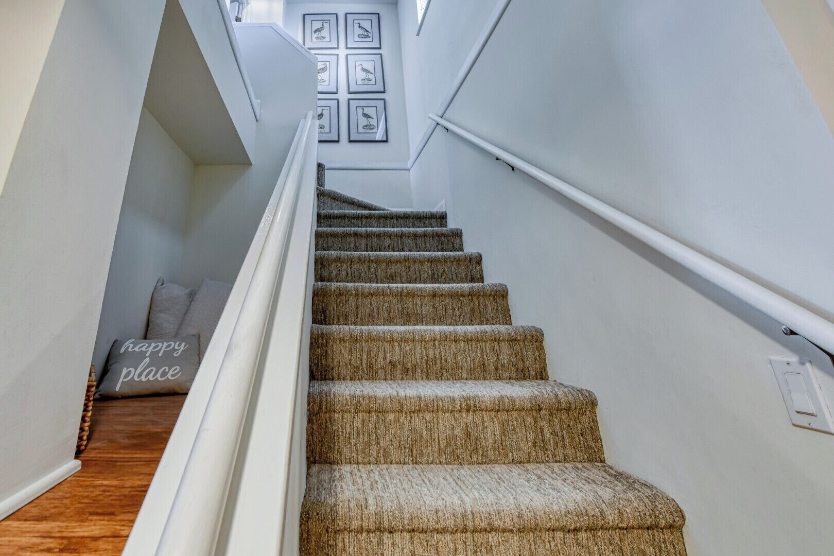 A staircase with a handrail, carpeted steps, and a 'happy place' pillow on the landing.