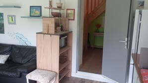 Ein Wohnzimmer mit einer schwarzen Ledersofa, einem Holzkabinett und einem kleinen Hocker. An den Wänden befinden sich Dekorationen und eine Tür, die in einen anderen Raum führt.