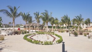 A landscaped area with palm trees, a circular garden, and a building with a thatched roof. - BAMBOO HAWANA Salalah - Forest Island  (Salalah)