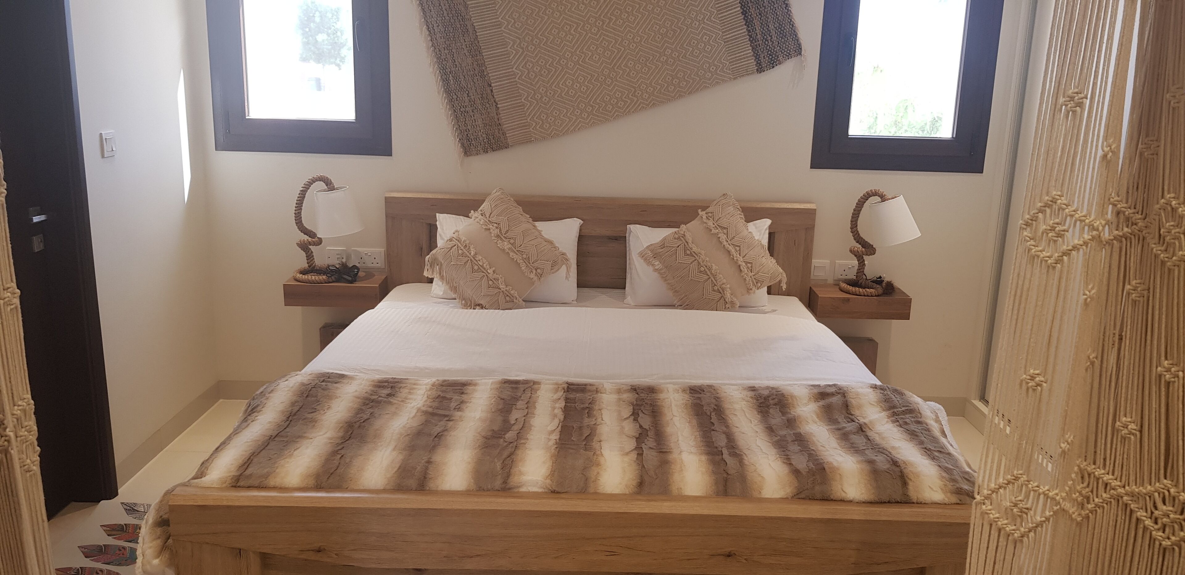 Un lit bien fait, recouvert d’une couverture à rayures, deux tables de chevet avec des lampes et un élément décoratif fixé au mur.