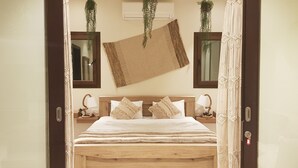 A bedroom with a wooden bed, two bedside tables with lamps, a hanging woven mat, and a mirror on the wall. - BAMBOO HAWANA Salalah - Forest Island  (Salalah)