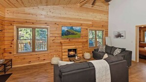 A log cabin interior with a fireplace, a sofa, and a television mounted on the wall.