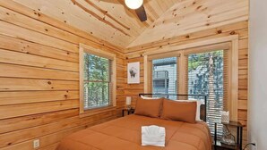 A wooden-paneled bedroom with a bed, a framed picture on the wall, and a window with blinds.