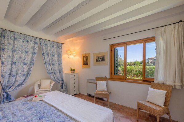 A bedroom with a bed, two chairs, a dresser, a window with a view, and wall-mounted lights.