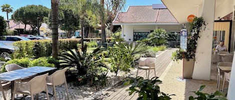 An outdoor patio area with tables and chairs, surrounded by lush greenery and palm trees.