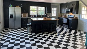 Una cocina con piso a cuadros blanco y negro, armarios oscuros, electrodomésticos de acero inoxidable y una isla central con taburetes.