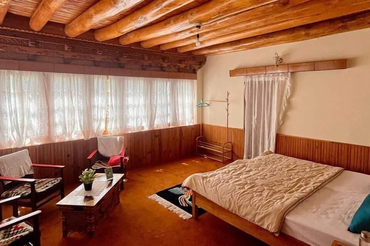 Una habitación acogedora con techo de madera, una cama, un escritorio, una silla y un ventanal con cortinas.