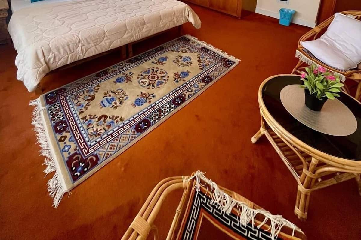 Un dormitorio con cama, un armario de madera, una mesita con una planta y una silla de mimbre.