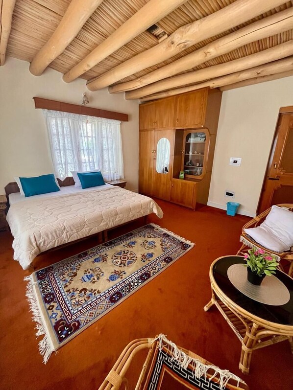 A bedroom with a bed, a wooden wardrobe, a small table with a plant, and a wicker chair. - Trinity Home Stay (Leh)