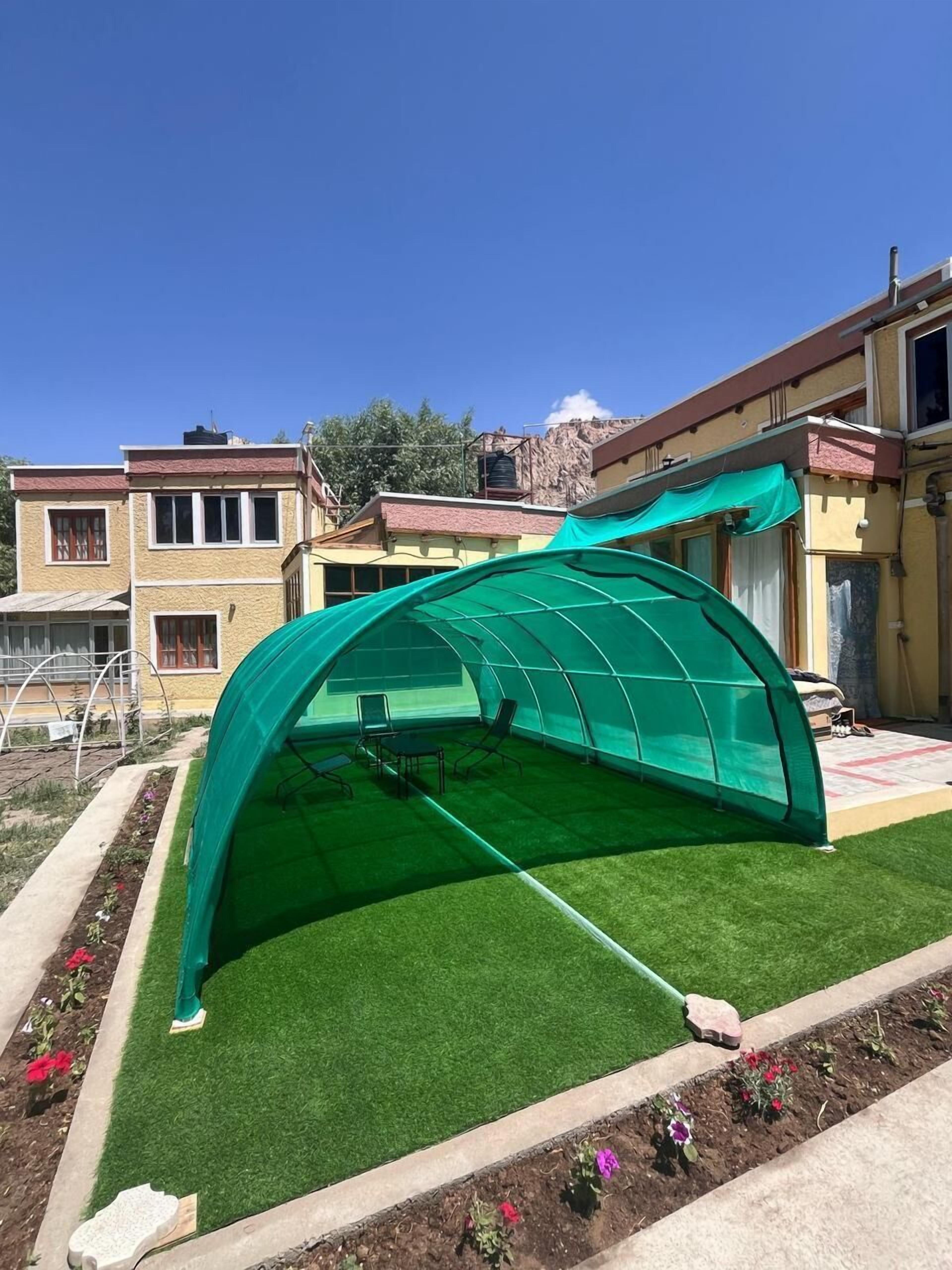A greenhouse structure with a curved roof, surrounded by a garden with artificial grass and flower beds.