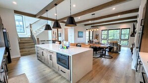 A spacious kitchen with a central island, wooden beams, pendant lighting, and a staircase leading to an upper level.