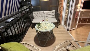 A small outdoor seating area with wicker chairs and a round table, a striped awning, and a sliding glass door.