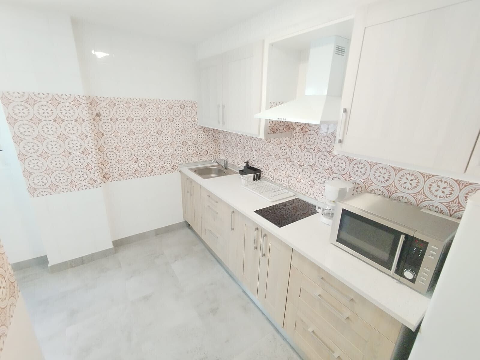 Una cucina moderna con zanzariera decorata, mobili bianchi, un forno a microonde e una macchina per il caffè.