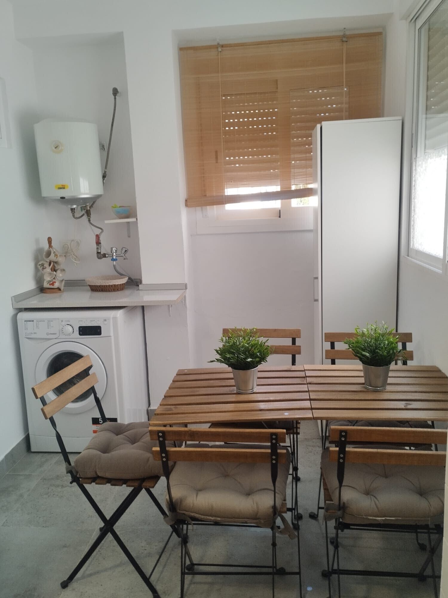 Cocina compacta con mesa, sillas, lavadora, refrigerador y una ventana con persianas.