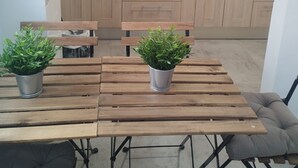 A compact kitchen with wooden cabinets, a microwave, a coffee maker, and a sink. There is a dining table with two potted plants and a bench with a cushion.