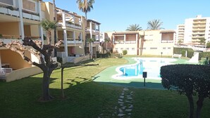 A pool area with a curved design, surrounded by well-maintained grass and palm trees. - JUNCOS 14  Solo Familias! (Xeraco Playa)