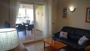 A living room with a black leather sofa, a wooden coffee table, and a lamp. There is a sliding glass door leading to an outdoor patio area with a table and chairs. - JUNCOS 14  Solo Familias! (Xeraco Playa)