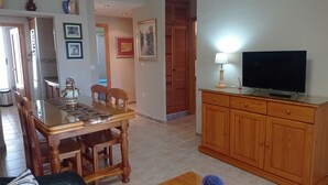 A dining area with a wooden table and chairs, a TV on a wooden cabinet, and a small potted plant on a table. - JUNCOS 14  Solo Familias! (Xeraco Playa)