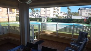 A balcony with a view of a swimming pool, outdoor furniture, and a clear sky. - JUNCOS 14  Solo Familias! (Xeraco Playa)