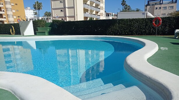 A swimming pool with a curved edge and a green deck area. - JUNCOS 14  Solo Familias! (Xeraco Playa)