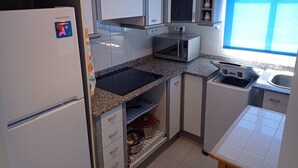 Eine kleine Küche mit Kühlschrank, Mikrowelle, Spüle und Schränken.