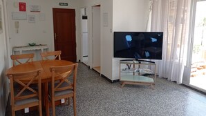 Ein Zimmer mit Fernseher auf einem Schrank, einem Holztisch mit Stühlen, einem kleinen Glastisch und einer Tür mit der Aufschrift 'SALIDA'.