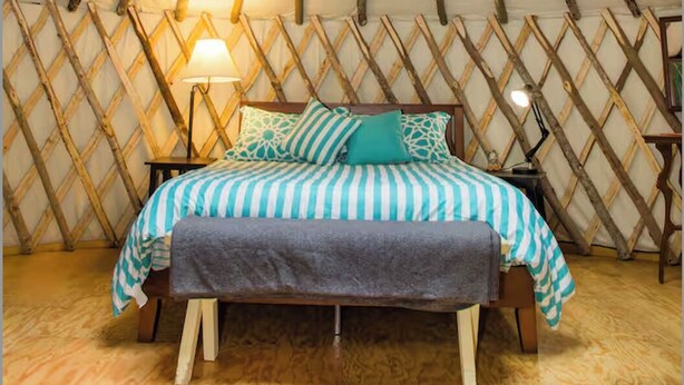 Acogedor interior de una yurta con una cama, una lámpara y una claraboya circular.