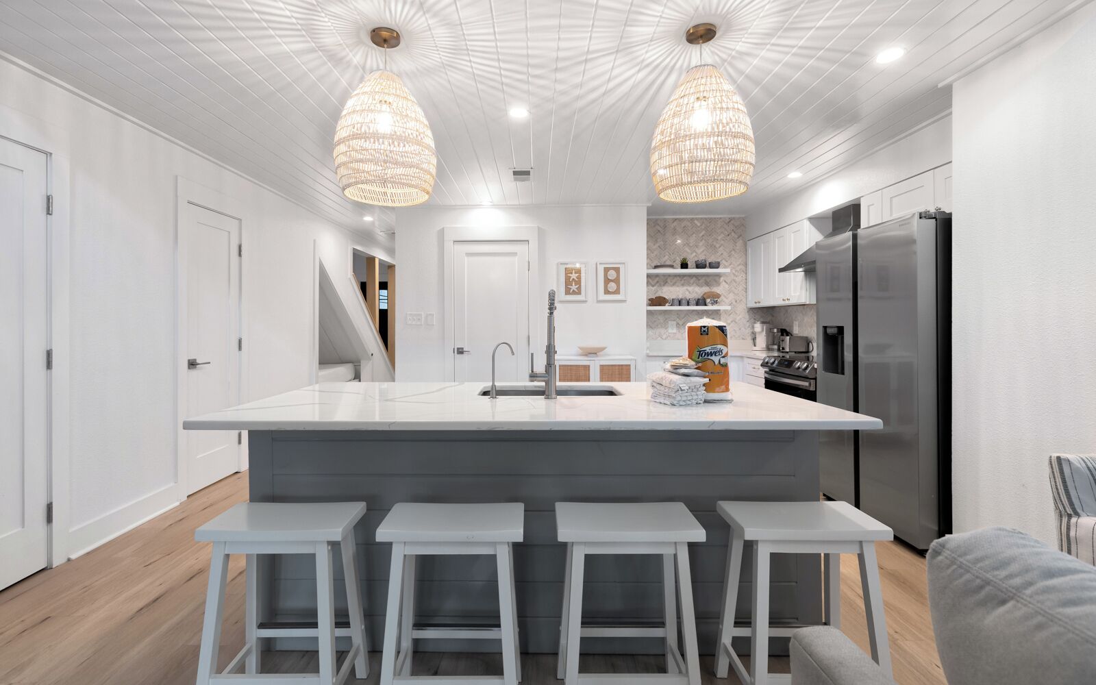 A modern kitchen with a central island, bar stools, a refrigerator, and pendant lighting.