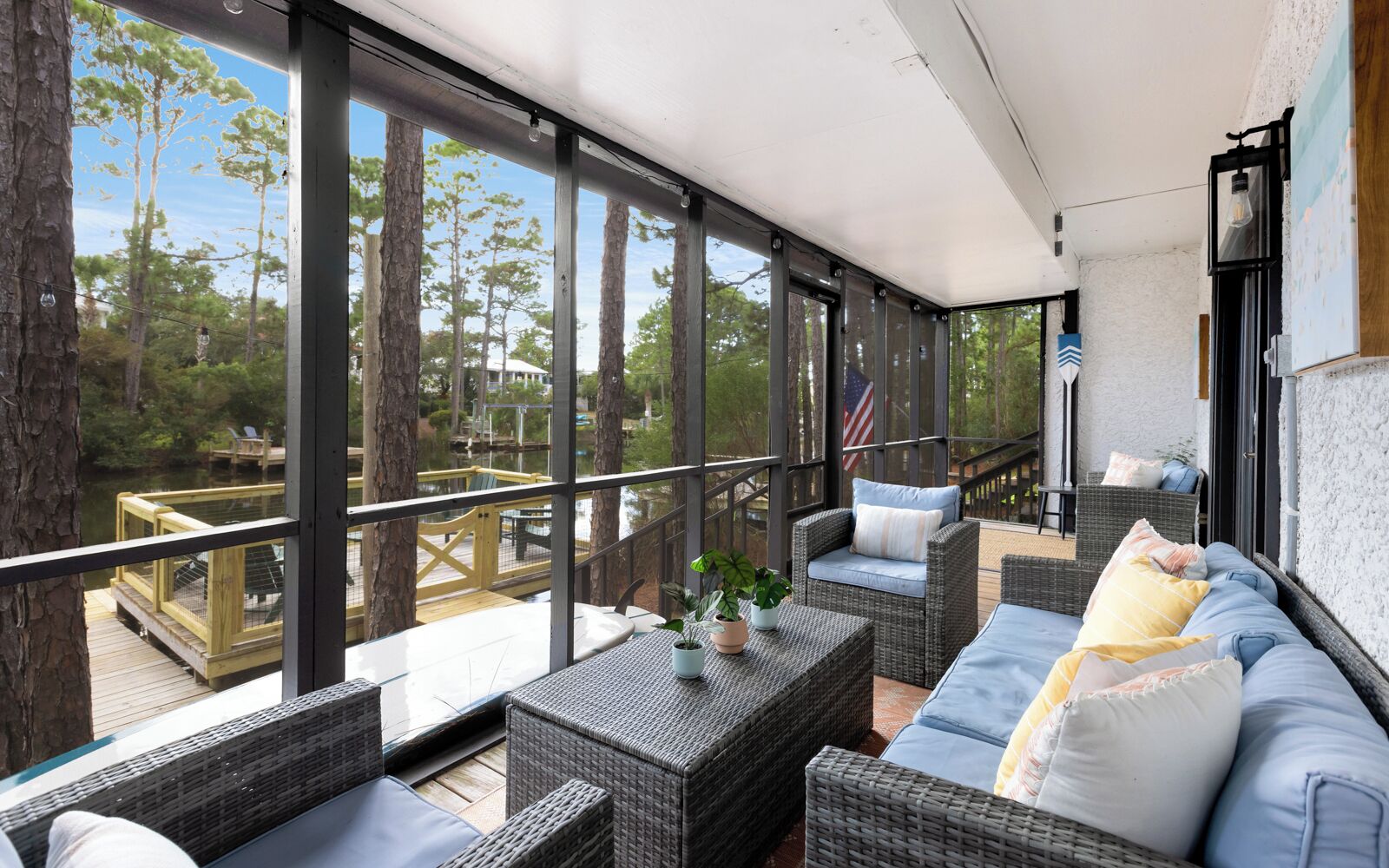 A covered outdoor seating area with wicker furniture, a view of trees and a dock, and an American flag.