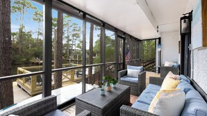 A covered outdoor seating area with wicker furniture, a view of trees and a dock, and an American flag. - Lakefront Home + Dock, Screened Patio, & Bikes (Santa Rosa Beach)