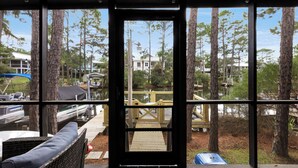 A view from a covered porch with a wooden deck, overlooking a dock with boats and a small house. - Lakefront Home + Dock, Screened Patio, & Bikes (Santa Rosa Beach)