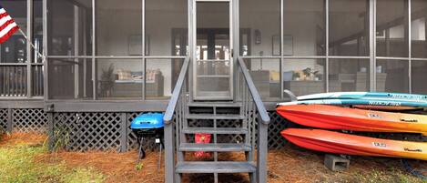 Un escalier en bois mène à une véranda grillagée où sont alignés plusieurs kayaks à l’extérieur.