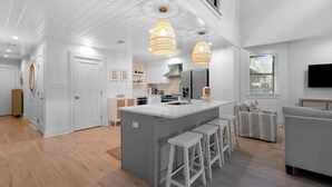 A modern kitchen with a central island, bar stools, pendant lighting, and a large window. - Lakefront Home + Dock, Screened Patio, & Bikes (Santa Rosa Beach)