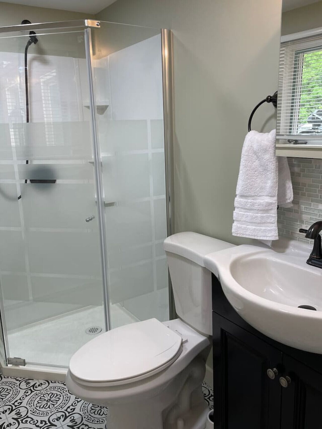 A bathroom with a glass shower enclosure, a white toilet, a white sink, and a black cabinet.
