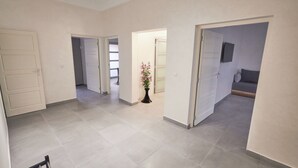 A spacious hallway with multiple doors leading to different rooms, a potted plant, and a flat-screen TV mounted on the wall.
