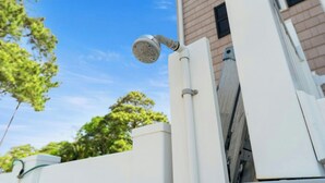 A white outdoor structure with a metal showerhead attached to a vertical pole.