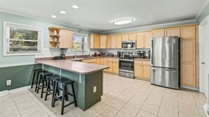 A modern kitchen with a central island, wooden cabinets, stainless steel appliances, and a window with blinds.
