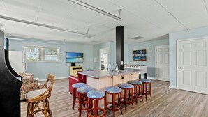 A spacious living area with a kitchen island, bar stools, and a television.