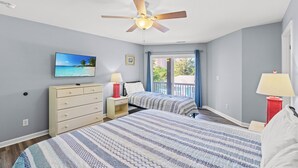 Une chambre avec deux lits, un ventilateur de plafond, une télévision et un balcon avec vue sur la plage.