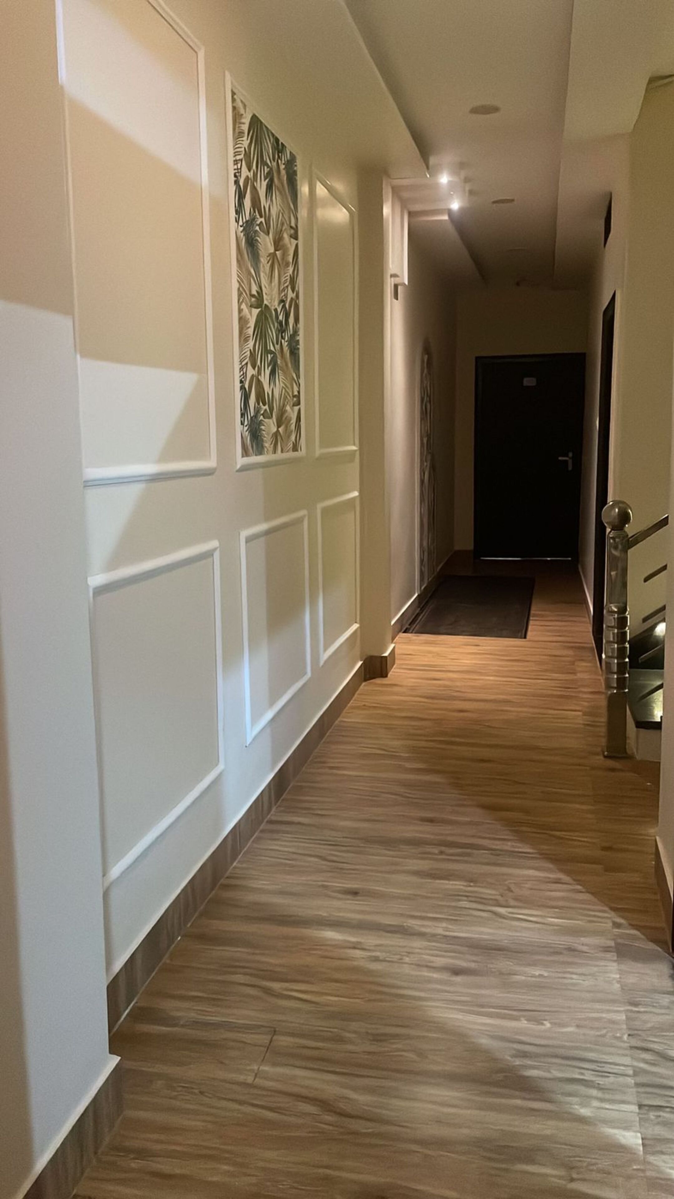 A hallway with wooden flooring, white walls, and a door at the end.