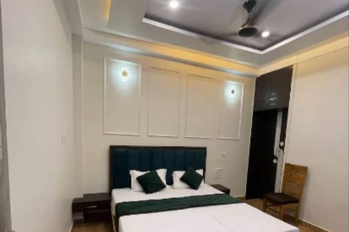 Une chambre moderne avec un plancher en bois, un grand lit avec une literie blanche et des oreillers verts, un ventilateur de plafond, un éclairage encastré et une tête de lit de couleur foncée.